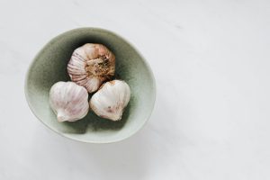 Bowl with garlic heads on white table