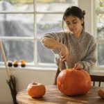 Woman in gray sweater carving orange pumpkin